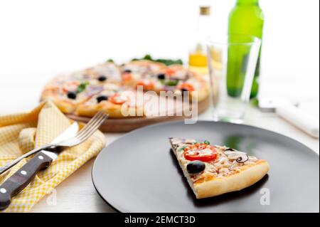 Frische Pizza im rustikalen italienischen Stil mit ruckigen Oliven Die Pilze und drei Arten des Käses auf dem hellen hölzernen Hintergrund mit einer Flasche kaltes Bier Stockfoto