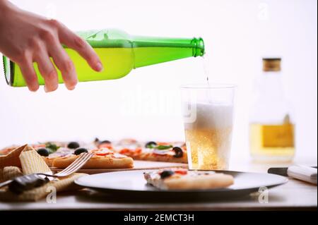 Frische Pizza im rustikalen italienischen Stil mit ruckigen Oliven Die Pilze und drei Arten des Käses auf dem hellen hölzernen Hintergrund mit einer Flasche kaltes Bier Stockfoto