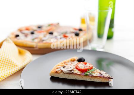 Frische Pizza im rustikalen italienischen Stil mit ruckigen Oliven Die Pilze und drei Arten des Käses auf dem hellen hölzernen Hintergrund mit einer Flasche kaltes Bier Stockfoto