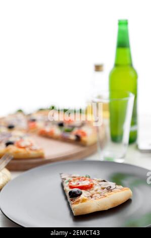 Frische Pizza im rustikalen italienischen Stil mit ruckigen Oliven Die Pilze und drei Arten des Käses auf dem hellen hölzernen Hintergrund mit einer Flasche kaltes Bier Stockfoto