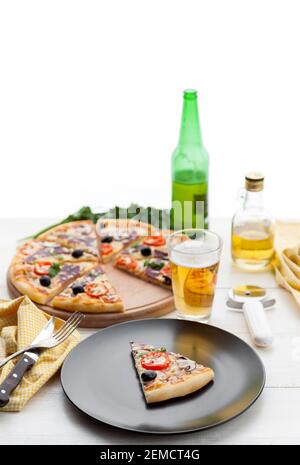 Frische Pizza im rustikalen italienischen Stil mit ruckigen Oliven Die Pilze und drei Arten des Käses auf dem hellen hölzernen Hintergrund mit einer Flasche kaltes Bier Stockfoto