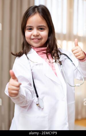 Portrait von lächelndem kleinen Mädchen gekleidet als Arzt geben Daumen nach oben. Stockfoto