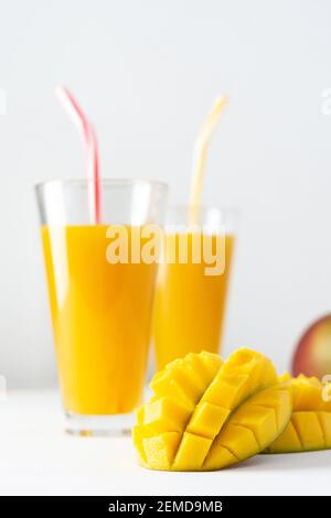 Mangosaft in Gläsern mit Saft und Stroh auf weißem Hintergrund, gehackte Mango und ganze, leckere gesunde süße natürliche Getränk Stockfoto