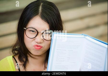 Asiatische Frau in Nerd Student Stil Lesung - Lifestyle-Porträt Von jungen süßen und glücklichen koreanischen Mädchen hält Buch auf Ihr Gesicht ist gelangweilt und verärgert Stockfoto