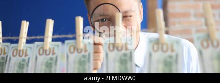 Der Mann schaut durch die Lupe auf hundert Dollarscheine, die auf Wäscheklammern hängen. Stockfoto