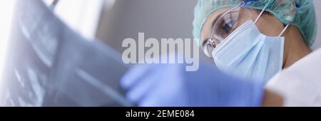 Arzt in schützender medizinischer Maske schaut auf eine Röntgenaufnahme. Stockfoto