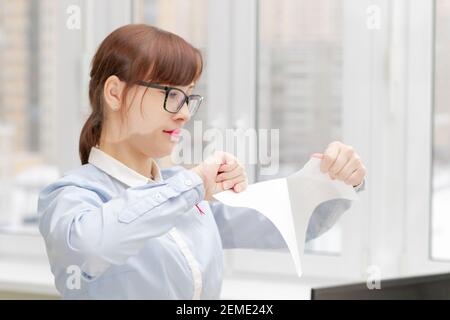 Junge hübsche Geschäftsfrau in streng stilvollen Kleidern und Brillen Im Büro in der Nähe des Desktops, um Dokumente zu zerrissen Stockfoto