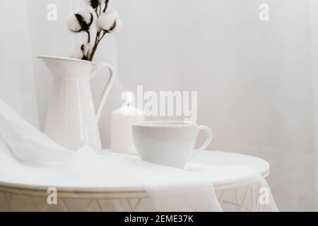 Details des Stilllebens im Wohnzimmer auf weißem Hintergrund. Tasse Kaffee, Baumwolle, Kerze, Vase. Moody. Platz für Text kopieren Stockfoto