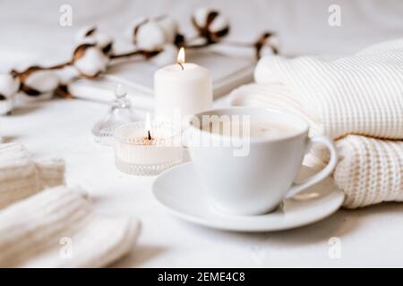 Details des Stilllebens im Wohnzimmer. Tasse Kaffee, Baumwolle, Buch, Kerze, Pullover. Moody. Gemütliches Herbst Winter Konzept auf weißen BA Stockfoto