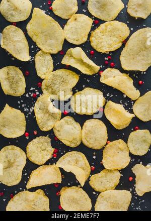Hintergrund für das Essen. Salzkartoffeln Chips. golden gebratenen Chips und Paprika auf schwarz . Schnell salzige Lebensmittel für Snack oder Party. Leckeres Essen für die Vorspeise. Tra Stockfoto