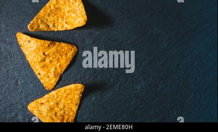 Food Hintergrund. Drei gelbe Dreieck geformte Tortilla Chips auf schwarz. Mexikanische salzige Snack Basis von Mais. Leckere Nachos für die Vorspeise. Traditionelle Crunc Stockfoto