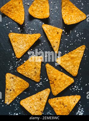 Hintergrund für das Essen. Gelbe dreieckige Tortilla Chips auf schwarz. Mexikanische salzige Snack Basis von Mais. Leckere Nachos als Vorspeise. Traditionelle knusprige Cor Stockfoto