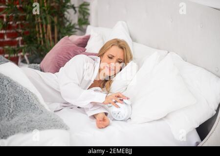 Verschlafene Frau im Bett mit Wecker Stockfoto