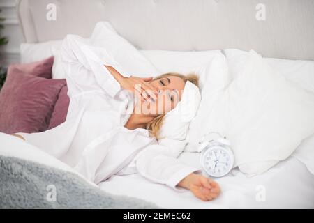 Gähnende Frau liegt im weißen Bett Stockfoto