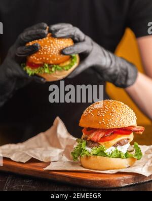 Helle saftige appetitliche Burger mit einem Cutlet, Käse, marinierte Gurken, Tomaten und Speck in den Händen eines Mädchens, ein Mädchen in speziellen Handschuhen für BU Stockfoto