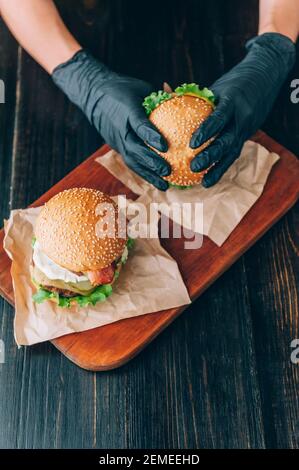 Helle saftige appetitliche Burger mit einem Cutlet, Käse, marinierte Gurken, Tomaten und Speck in den Händen eines Mädchens, ein Mädchen in speziellen Handschuhen für BU Stockfoto