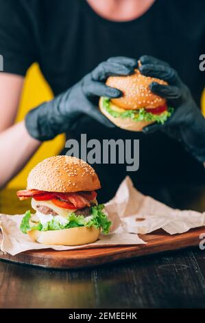 Helle saftige appetitliche Burger mit einem Cutlet, Käse, marinierte Gurken, Tomaten und Speck in den Händen eines Mädchens, ein Mädchen in speziellen Handschuhen für BU Stockfoto