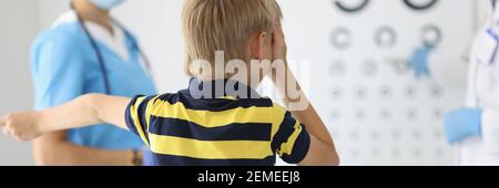 Boy sitzt mit dem Rücken beim Augenarzt Termin, schaut auf Tisch und beantwortet Fragen. Stockfoto