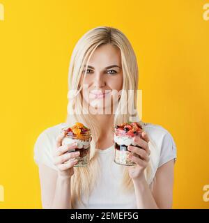 Schöne junge gesunde Mädchen auf hellen sonnigen Hintergrund mit Gläsern in den Händen. In Gläsern Haferbrei Haferbrei und Müsli mit Früchten Beeren und Getreide Stockfoto