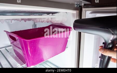 Abtauvorgang von Eis in einem heimischen Gefrierschrank. Sammeln von Wasser in einem Kunststoffbecken. Stockfoto