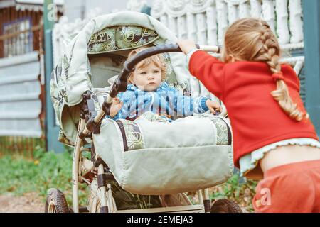 Schwester spielt mit ihrem Bruder im Kinderwagen, rollt das Baby die Straße hinunter Stockfoto