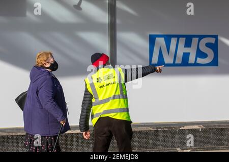 Mann zeigt auf das Covid-Testzentrum in Preston, Lancashire. Februar 2021. Freiwillige, die im NHS Covid 19 Impfzentrum helfen. Nationale Impfprogramme im Vereinigten Königreich, in denen die gemeldete Impfstoffaufnahme in Gebieten mit einem höheren Anteil an ethnischen Minderheiten, die weniger wahrscheinlich einen Coronavirus-Jab einnehmen, geringer war. Stockfoto