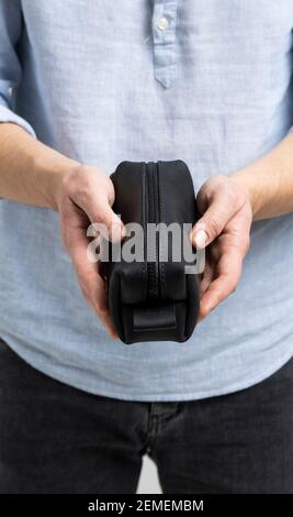 Herren-Kosmetiktasche aus schwarzem Leder oder Tasche für Toilettenartikel in Herrenhänden in blauem Hemd. Stil, Retro, Mode, Vintage und Eleganz. Stockfoto