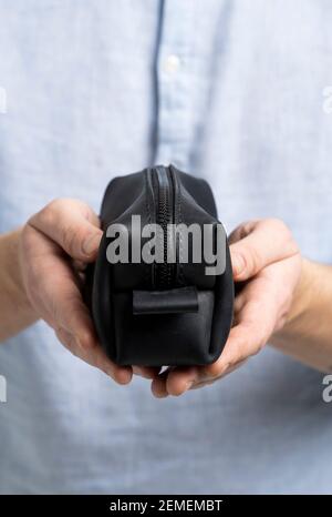 Herren-Kosmetiktasche aus schwarzem Leder oder Tasche für Toilettenartikel in Herrenhänden in blauem Hemd. Stil, Retro, Mode, Vintage und Eleganz. Stockfoto