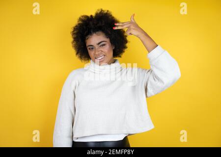 afroamerikanische Frau trägt lässigen Pullover über gelben Hintergrund Schießen und sich selbst töten Zeigen Hand und Finger an den Kopf wie Waffe, Selbstmord Stockfoto