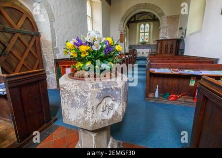 Das Innere der kleinen, historischen Wisley Kirche, eine normannische Kirche aus dem 12th. Jahrhundert in Wisley Dorf, und Steinfont mit Blumen, Surrey, Südostengland Stockfoto