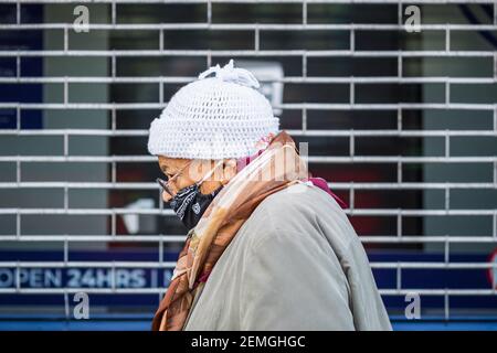 London, Großbritannien - 5. Februar 2021 - eine ältere Frau mit einer schützenden Gesichtsmaske, die an einem geschlossenen Geschäft in der Wood Green High Street vorbeikommt Stockfoto