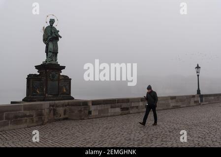 Prag, Tschechische Republik. Februar 2021, 25th. Ein Mann mit Gesichtsmaske als vorbeugende Maßnahme gegen die Ausbreitung des Coronavirus läuft an einem nebligen Morgen entlang einer leeren Karlsbrücke in Prag. Ab heute ist das Tragen einer FFP2 Maske in Geschäften und öffentlichen Verkehrsmitteln in der Tschechischen Republik obligatorisch. Kredit: SOPA Images Limited/Alamy Live Nachrichten Stockfoto