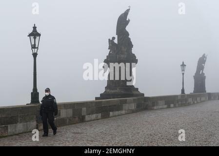 Prag, Tschechische Republik. Februar 2021, 25th. Eine Polizistin mit Gesichtsmaske als vorbeugende Maßnahme gegen die Ausbreitung des Coronavirus läuft an einem nebligen Morgen entlang einer leeren Karlsbrücke in Prag. Ab heute ist das Tragen einer FFP2 Maske in Geschäften und öffentlichen Verkehrsmitteln in der Tschechischen Republik obligatorisch. Kredit: SOPA Images Limited/Alamy Live Nachrichten Stockfoto