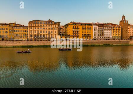 Schöner Blick auf das Ufer des Arno entlang der Straße Lungarno degli Acciaiuoli in der Altstadt von Florenz in der Abenddämmerung. Zwei alte Florentiner Gondelboote, so... Stockfoto