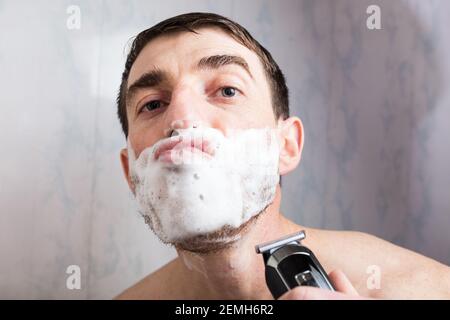 Mann mit lustigen niedlichen Gesicht in Schaum für die Rasur und elektrische Trimmer in der Hand. Stockfoto