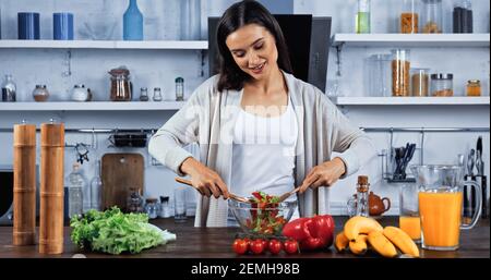 Lächelnde Frau, die frischen Salat in der Küche mischte, nahe Orangensaft Tabelle Stockfoto