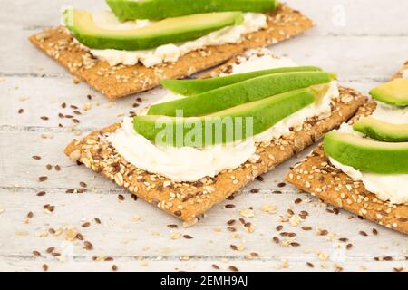 Sandwiches mit Crackern, Käse und Avocado auf grauem Holzhintergrund. Stockfoto