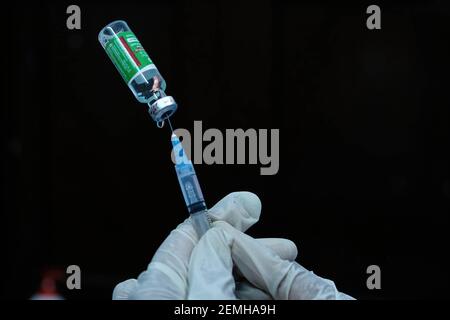 Im Madhyamgram Hospital wird eine Handfläche mit Handschuhen mit einer Spritze und einer Covishield Coronavirus-Impfstoffflasche gesehen. Menschen über 60 Jahren und 45-Jährige mit Begleiterkrankungen können den Impfstoff ab dem 1st. März auf eigene Kosten in Privatkliniken erhalten. Stockfoto