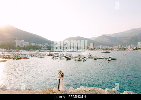 Die Braut und Bräutigam umarmen und küssen am Strand Vor dem Hintergrund der Bootsanlegestelle in Budva Stockfoto