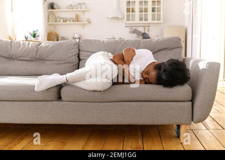 Depressive unglückliche afrikanische Frau, die zu Hause auf der Couch liegt, weint, an Scheidung leidet oder aufbricht. Stockfoto
