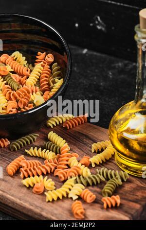 Schüssel mit bunten Fusilli Pasta und eine Flasche Öl auf Dunkler Tisch Stockfoto