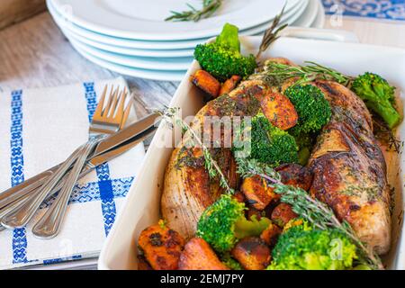 mediterranes Schweinefleischgericht mit Filet, gerösteten Süßkartoffeln und Brokkoli, serviert mit Kräuterbutter in einer Kasserolle auf einem Tisch mit Ferkeln und Forkes Stockfoto