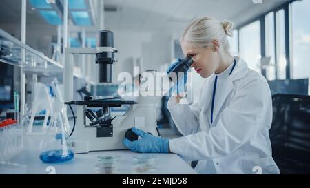 Modernes medizinisches Forschungslabor: Portrait einer Wissenschaftlerin, die unter dem Mikroskop schaut und Biochemikalien analysiert. Advanced Scientific Lab für Stockfoto