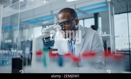 Modern Medical Research Laboratory: Portrait of Male Scientist looking under Microscope, analysing Samples. Fortgeschrittenes wissenschaftliches Labor für Medizin Stockfoto