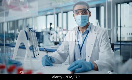 Medical Research Laboratory: Portrait of Male Scientist Tragen Gesichtsmaske Blick auf Kamera, Aufschreiben von Informationen. Advanced Scientific Lab für Stockfoto