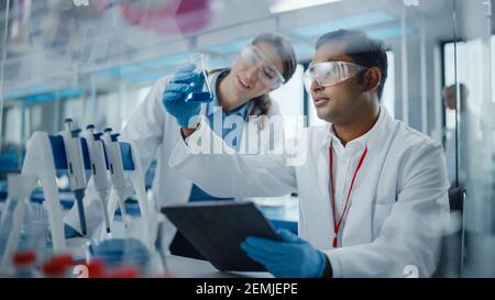 Modernes medizinisches Forschungslabor: Zwei Wissenschaftler arbeiten zusammen, analysieren Chemikalien in Laborflask, diskutieren Problem. Advanced Scientific Stockfoto