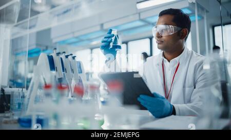 Medical Research Laboratory: Portrait eines gutaussehenden männlichen Wissenschaftlers mit digitalen Tablet-Computer, Analyse von flüssigen Biochemikalien in einem Laborflask Stockfoto