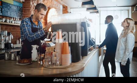 Der gutaussehende Barista im karierten Hemd macht einen Latte für einen Kunden in einer Café-Bar. Schöne kaukasische männliche Kassierer arbeitet in einem gemütlichen Loft Stockfoto