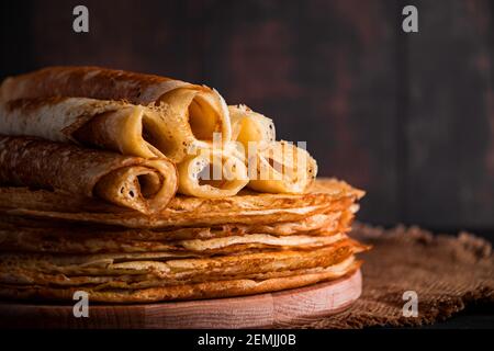 Traditionelles russisches Essen - dünne Pfannkuchen. Ein Stapel Crepes auf einem dunkelbraunen Holzhintergrund. Rustikaler Stil, Platz für Text. Stockfoto