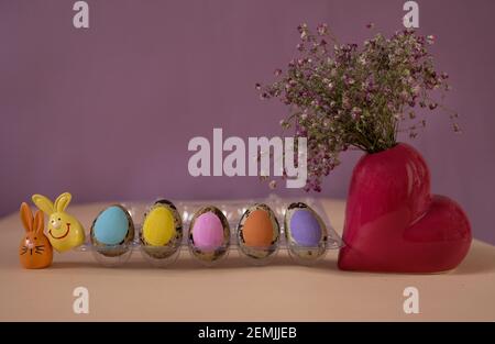 Bunte Pastell-Osterschwanzeier in einer Reihe, zwei Souvenir-Hasen, eine herzförmige Vase mit rosa Gypsophila. Platz für Text, Worte. Osterdekor Stockfoto